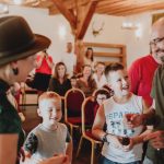 A lively indoor gathering with adults and children enjoying a friendly interaction in a warmly lit room.